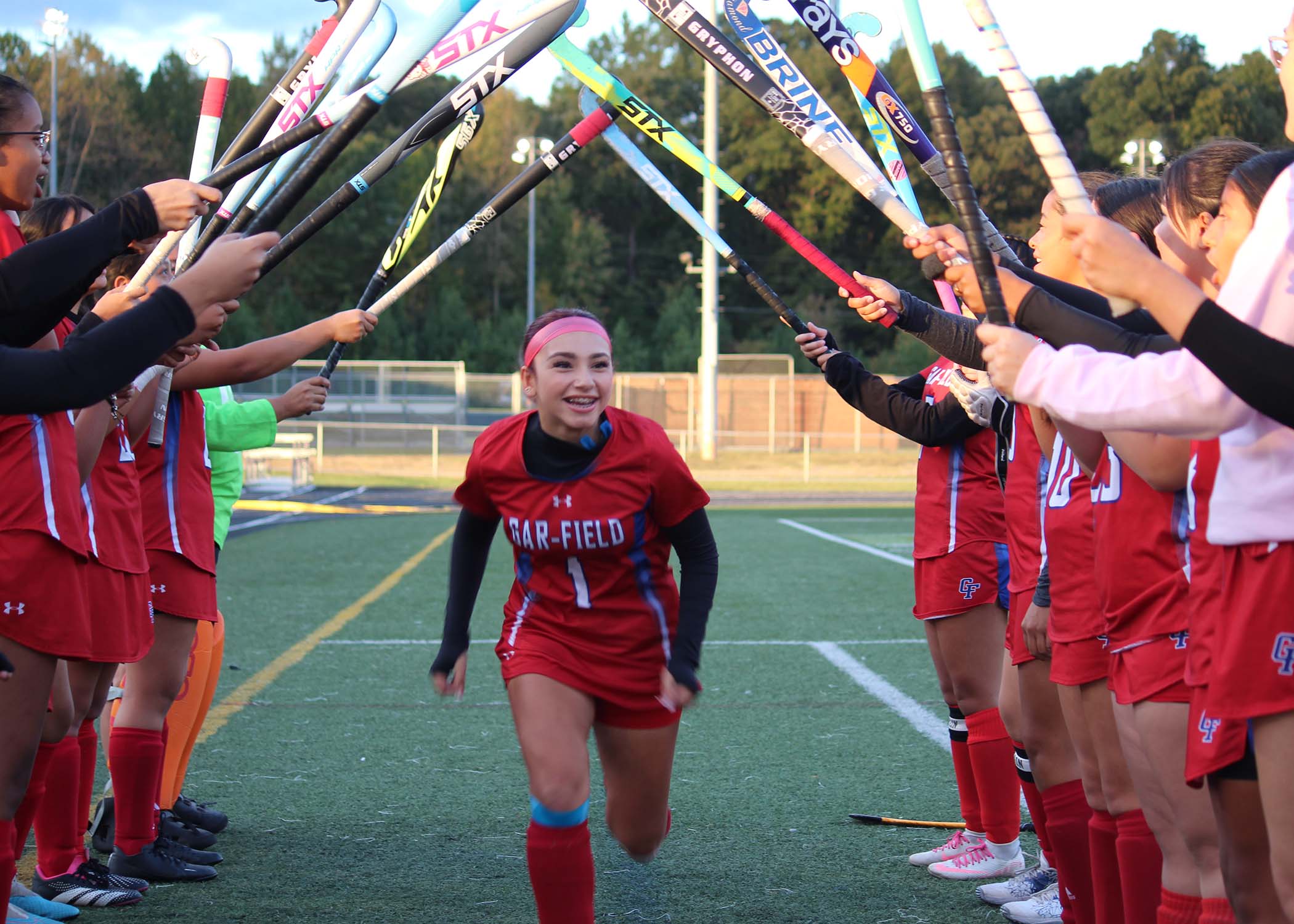Athlete running through tunnel of teammates field hockey sticks