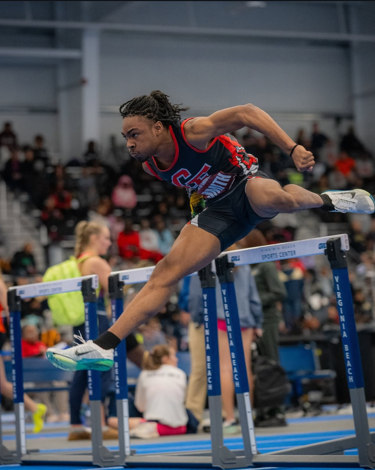 Male student athlete hurdling at an indoor track meet