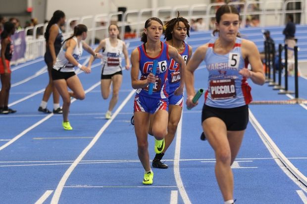 2 Female student athletes running in a race at an indoor track meet